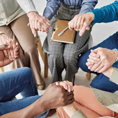 Menschen, die im Kreis sitzen, halten sich an den Händen
